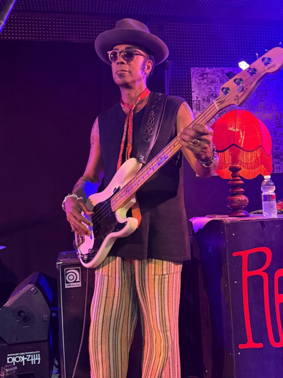 Al Berry playing a white bass onstage in striped trousers