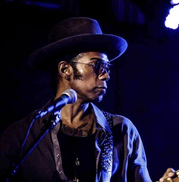 Al Berry in a wide-brimmed hat and sunglasses under blue stage light